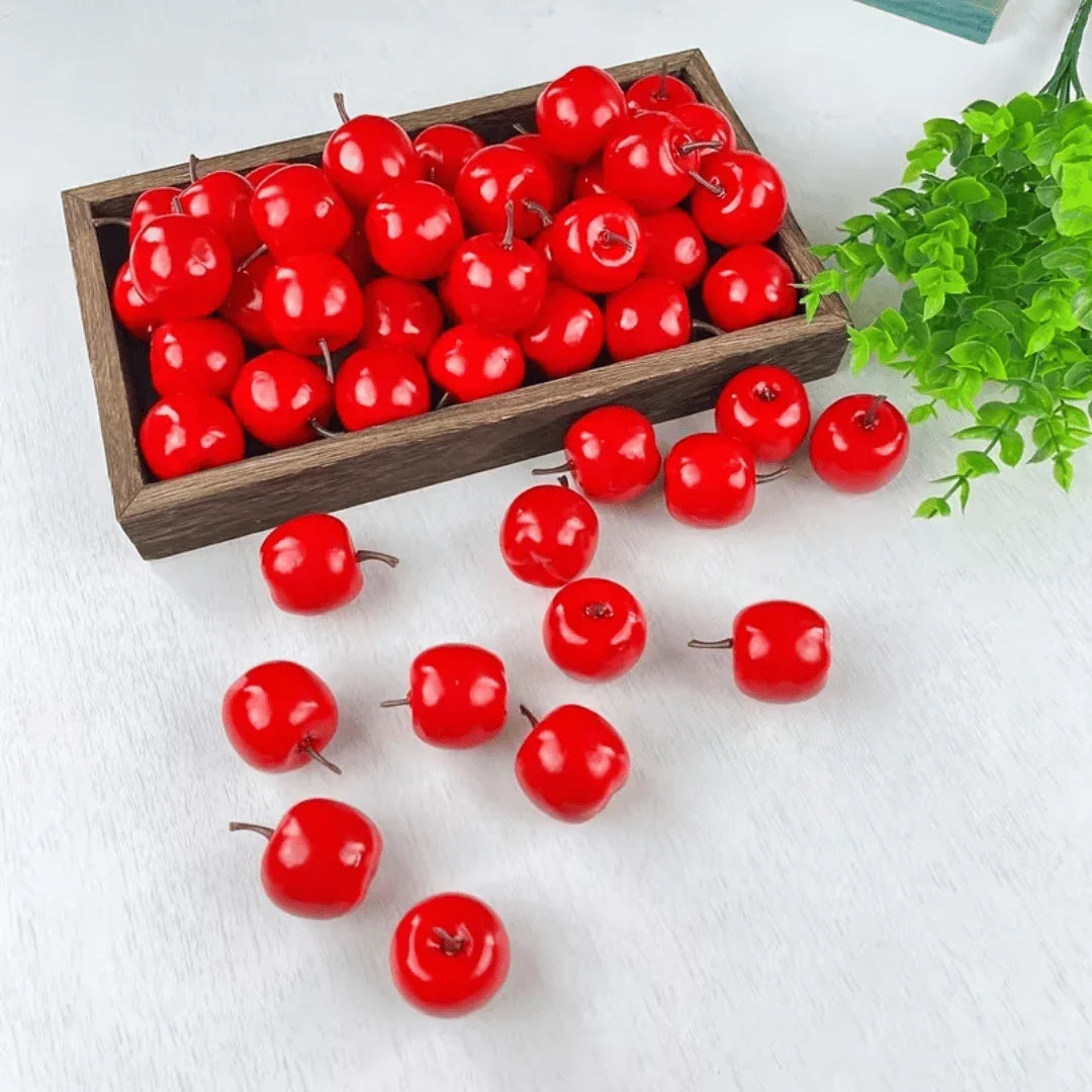 Artificial red cherries in a rustic wooden tray and scattered on a white surface