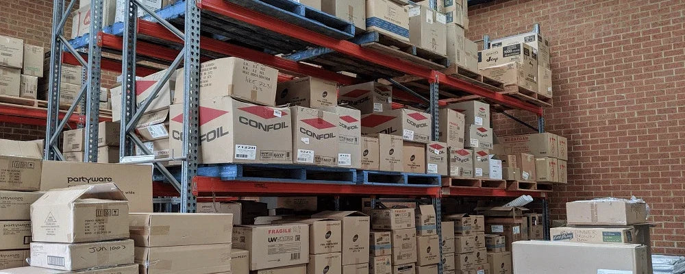 Stacked cardboard boxes of catering and packaging supplies on warehouse shelving.