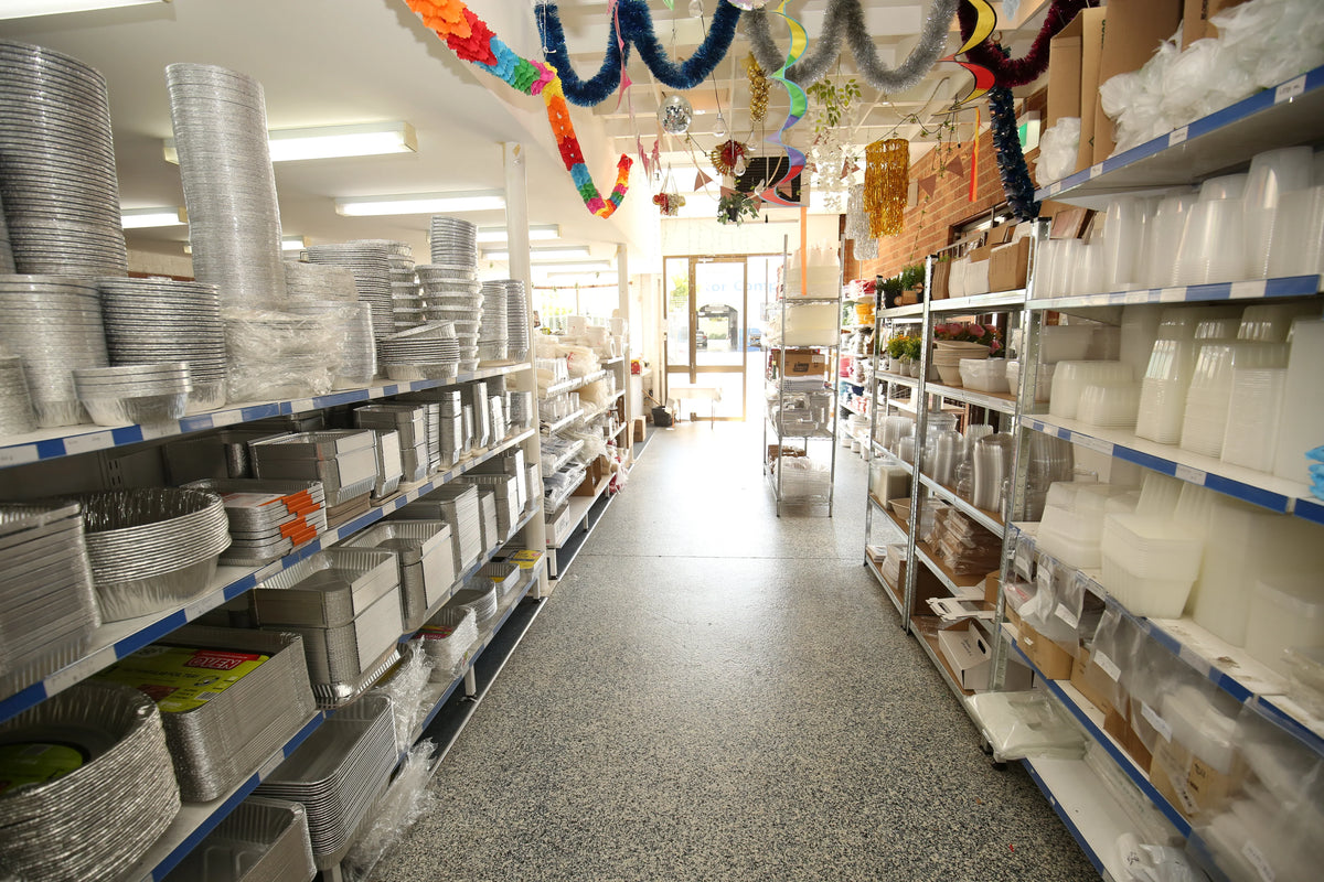 A store aisle featuring shelves stocked with disposable aluminum trays and plasticware.