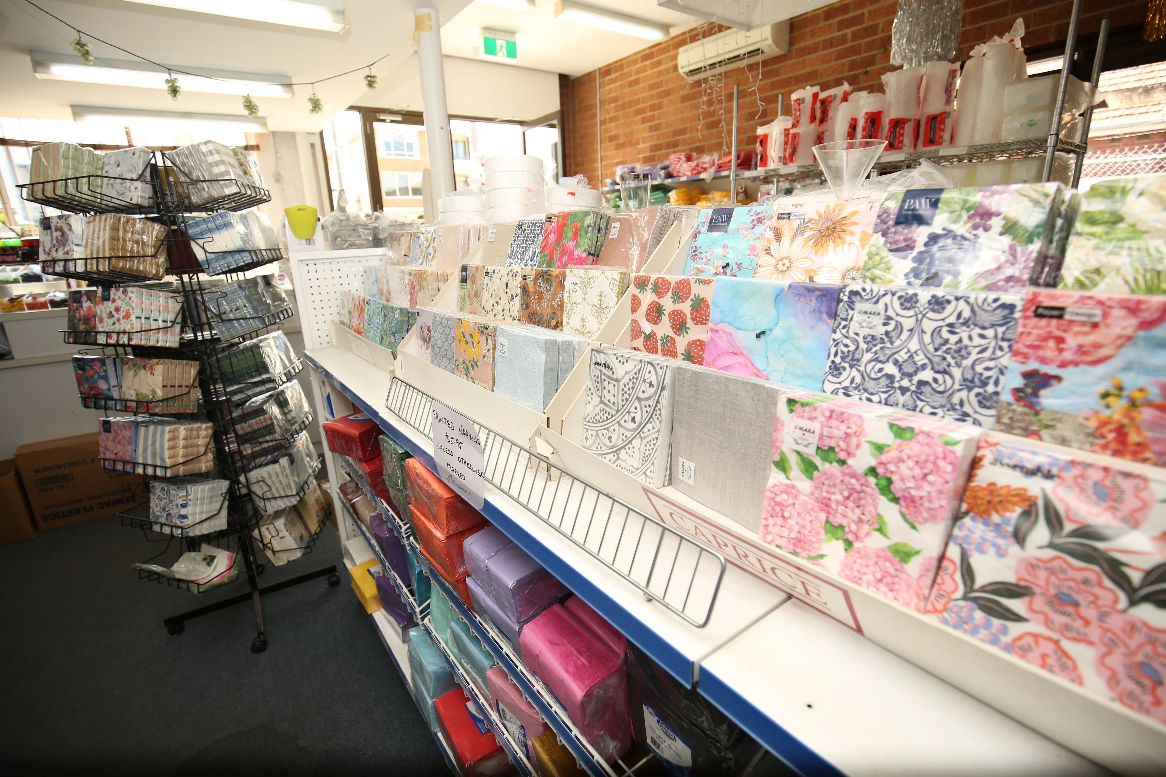 Assorted patterned paper napkins displayed on retail shelves and a rotating rack.