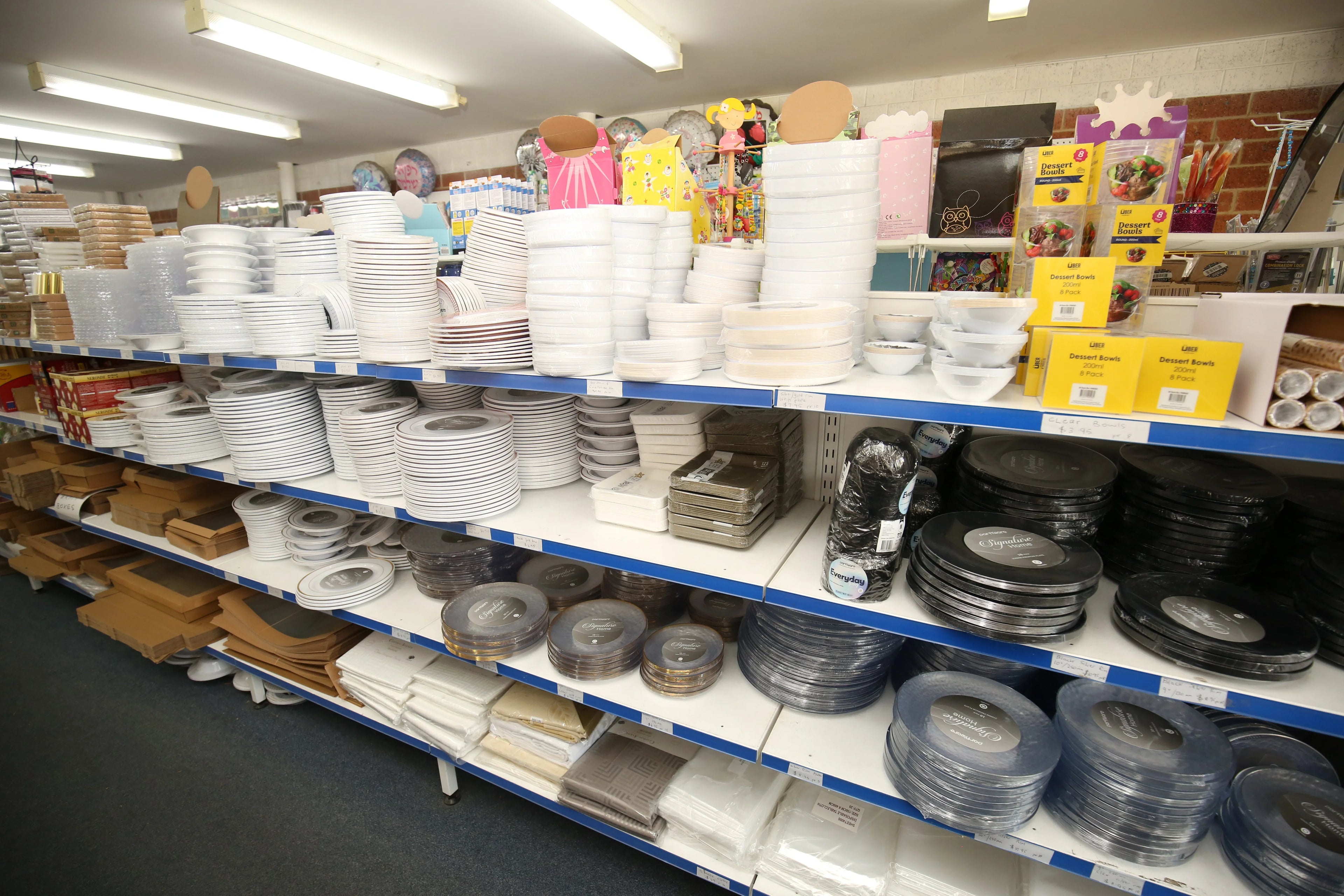 Retail shelves stocked with wholesale disposable white and black plastic plates and bowls.