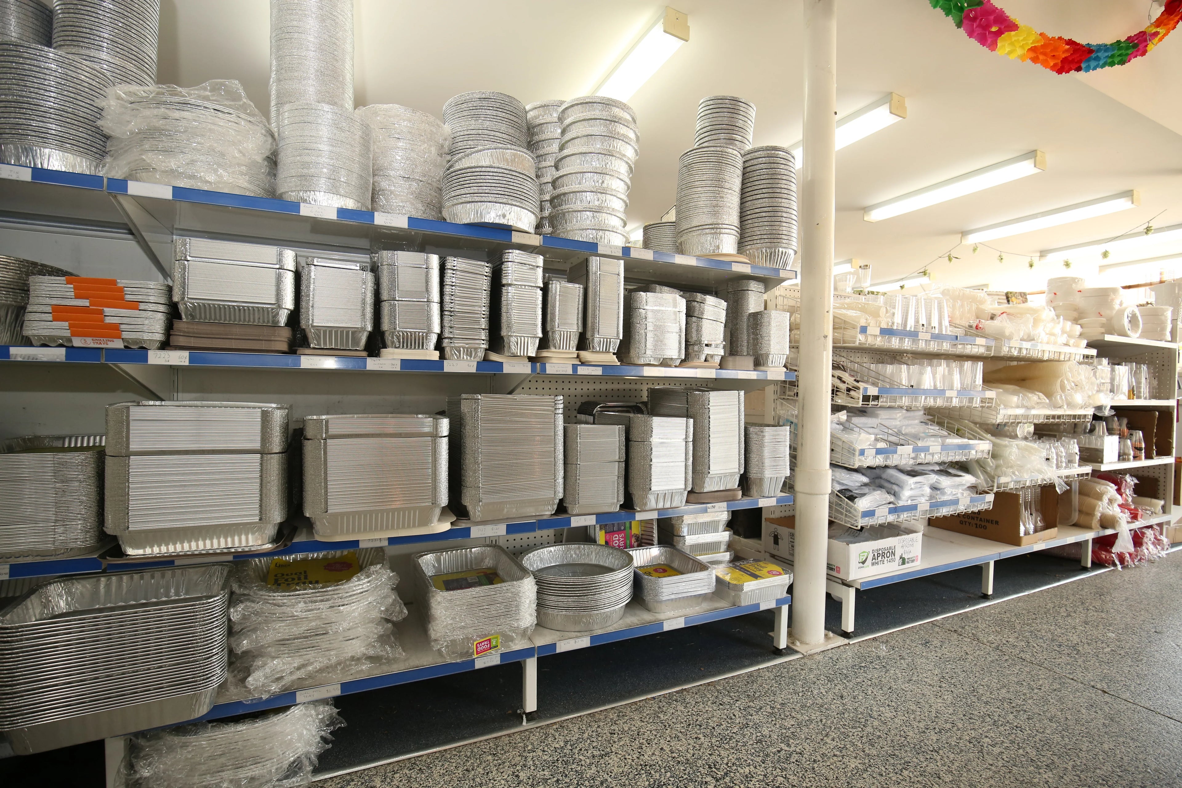 Variety of disposable aluminum foil catering trays and containers on store shelves.
