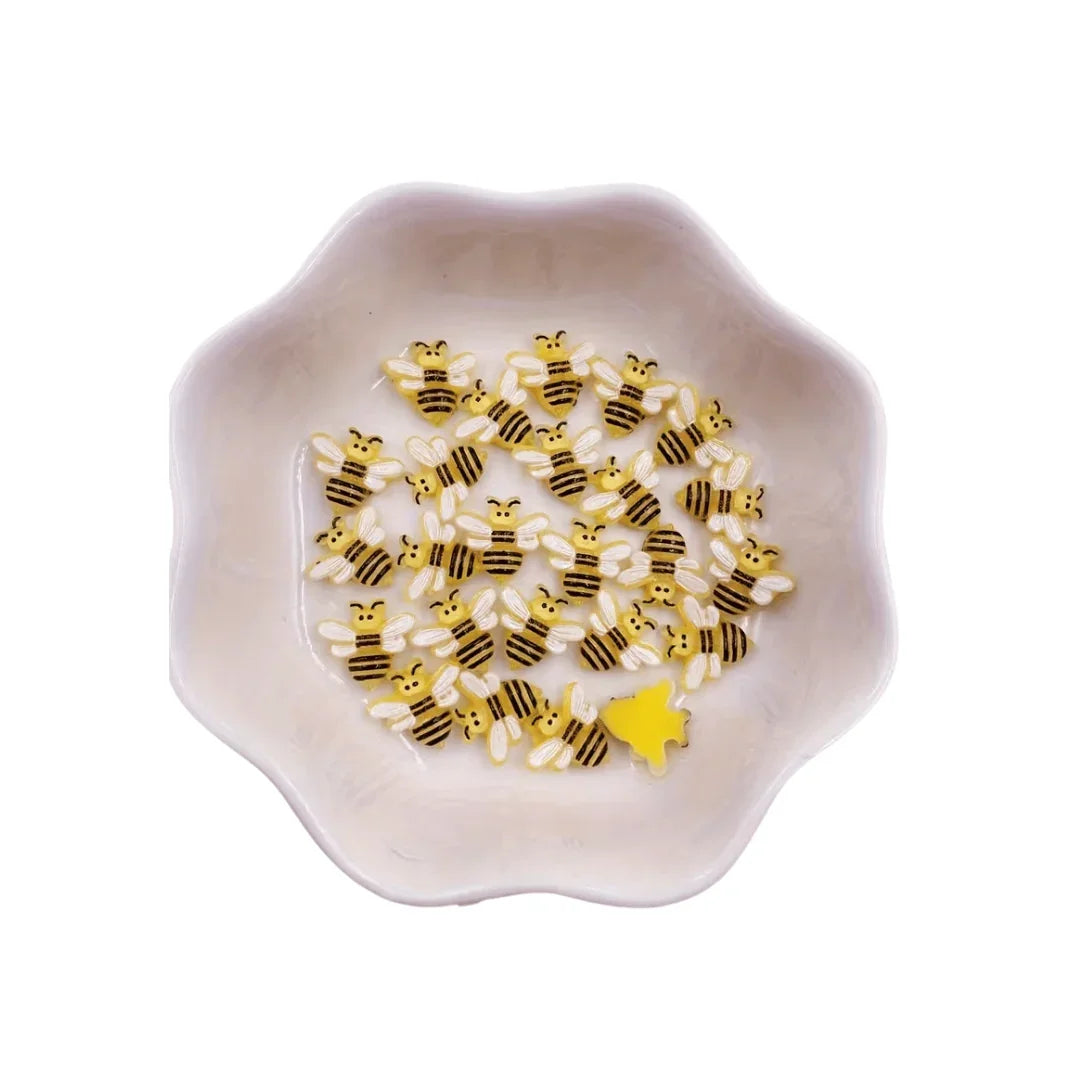 Small yellow and black bee-shaped confetti in a white scalloped decorative bowl