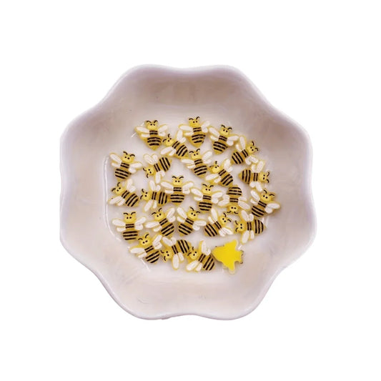 Small yellow and black bee-shaped confetti in a white scalloped decorative bowl