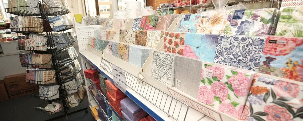 Variety of patterned paper napkins and disposable catering supplies on retail display shelves